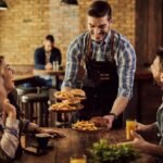 happy-waiter-serving-food-group-cheerful-friends-pub_637285-12525
