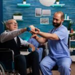 practitioner-man-doctor-helping-retiree-senior-male-wheelchair-physiotherapy-strength-exercise_482257-12761